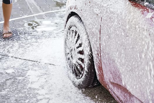 Red car washed in self serve carwash, detail on white soap foam spraying from high pressure hose onto wheel