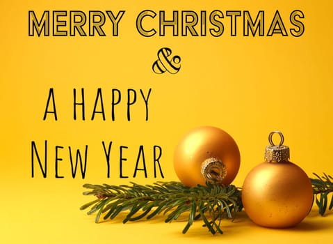 Merry Christmas and a happy New Year with two golden vintage Christmas baubles and am fir tree twig on a yellow background, holiday greetings