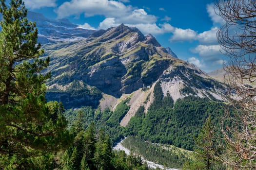 A mountain range with a river running through it. The sky is blue and the mountains are covered in trees