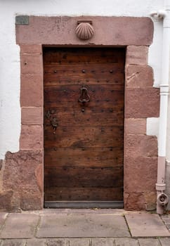 A wooden door with a shell-shaped knob. The door is located in front of a stone wall
