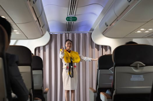 Cabin crew presenting a life jacket vest on board before the flight departure and showing the direction of emergency exits