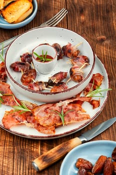 Homemade sweet and savory bacon wrapped dates served on a platter. Rustic style.