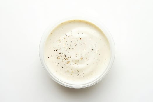 A smooth and creamy Caesar dressing is displayed in a glass bowl, topped with freshly ground black pepper. The simple white background enhances the dressings texture and color.