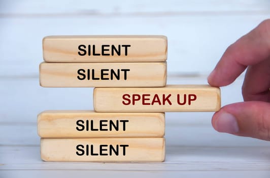 Speak up and silent text on wooden block with hand pulling the wooden block with speak up text. Speak up and courage concept.