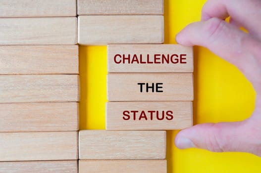 Hand pulling out wooden blocks with Challenge the Status text on yellow background
