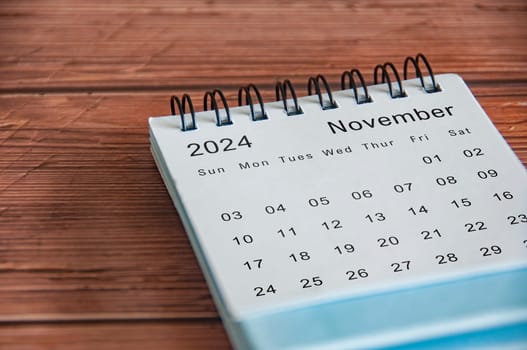 Side view of November 2024 table calendar on wooden cover background.