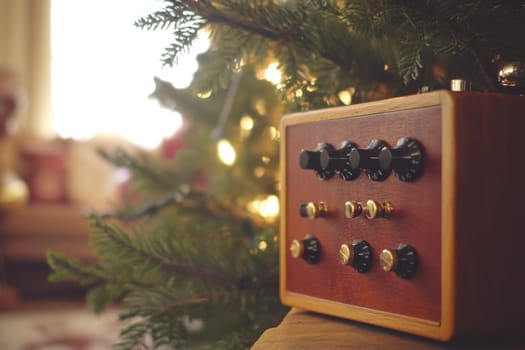 A vintage wooden music box sits next to a Christmas tree adorned with twinkling lights and pine branches creating a cozy atmosphere.