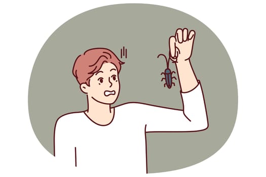 Man with bug in hand, looks at insect and gets scared suffering from arachnophobia and disgust. Guy found bug and wants to get rid of pest by calling service for chemical treatment of insects