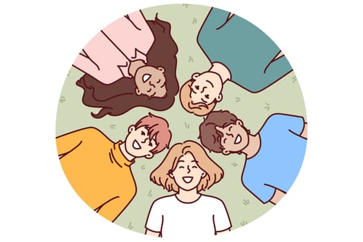 Happy children lie on green grass and smile while enjoying walk in park in hot summer weather. Top view of faces of multiethnic children boys and girls lying in clearing on sunny day