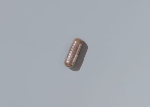 Brown medical capsule on grey top view, hard shadows. Preventive medicine and healthcare, taking dietary supplements and vitamins. Minimal composition