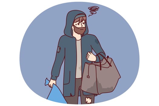 Man tramp with bag walks city streets in search of shelter or food thrown into trash. Concept of helping homeless and people in distress in need of shelter or food stamps for survival