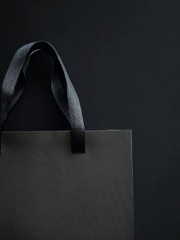 A sleek black shopping bag with textured handles, set against a dark background, providing ample copy space.