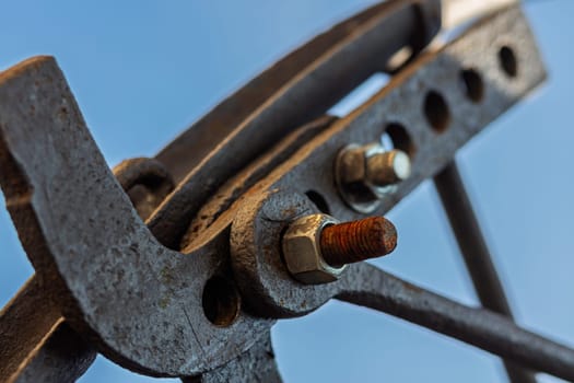 Rusty metal clamp holding construction elements together with visible threaded connection and a blue sky in the background