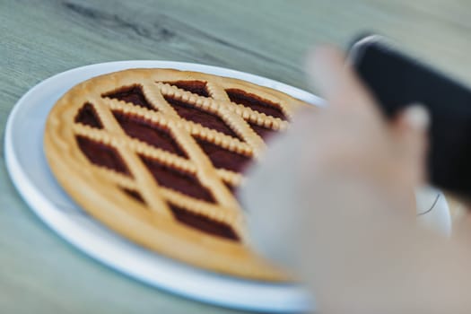 Woman is taking a picture of a freshly baked pie using her smartphone, capturing the moment before enjoying her delicious creation