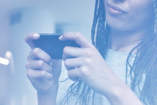 Young woman using her smartphone at home, scrolling through social media and checking messages, with natural light highlighting her hands and stylish jewelry