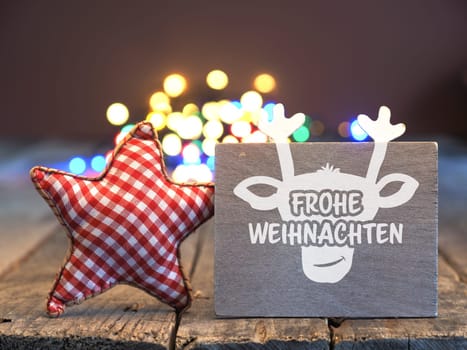 A wooden sign with a reindeer face and the German words Merry Christmas against a blurry light background, seasonal holiday concept, Christmas card
