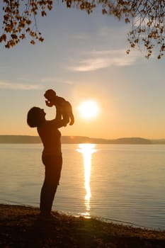 A heartwarming silhouette depicting a loving parent lifting a cheerful child at sunset beside the tranquil water