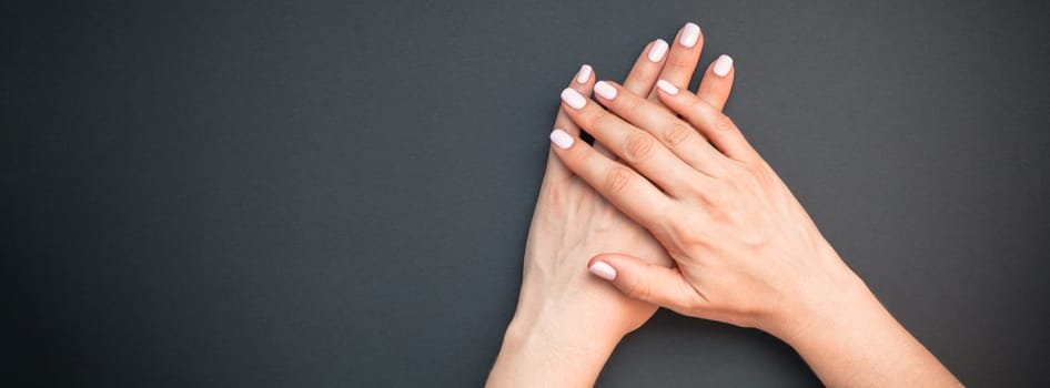 Stylish trendy female pastel pink manicure. Beautiful young woman's hands on black background. Beauty and SPA concept. Template for feminine blog social media