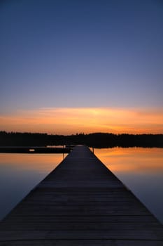 Wooden jetty at sunset on a Swedish lake. The colors of the sunset are reflected in the water. A bathing lake in the Scandinavian countryside