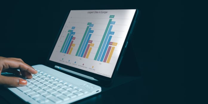 Woman hand using tablet reviewing data in financial charts and graphs with tablet, Business analyzing graphic diagrams for statistic revenue during remote working on tablet.