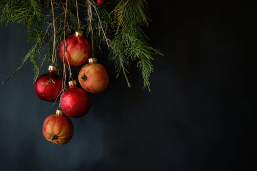 Red ornaments and apples hang from pine branches against a dark backdrop creating a festive and cozy holiday atmosphere.