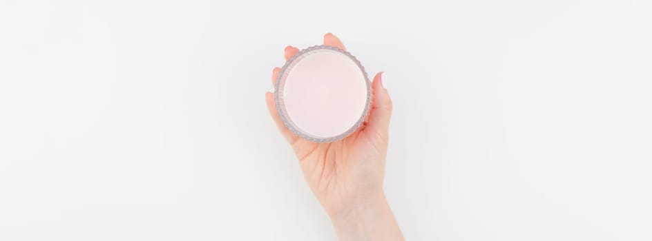 Woman hand with pastel manicure polish holding pink aromatic candle isolated on white background with copy space. Long wide banner for feminine beauty blog social media. Spa and wellness concept