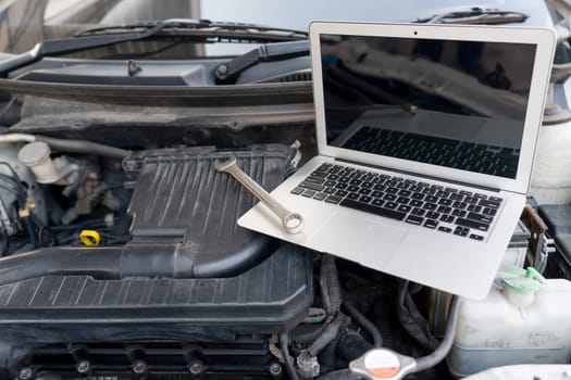Laptop computer and wrench tool placing inside car's hood on car engine.