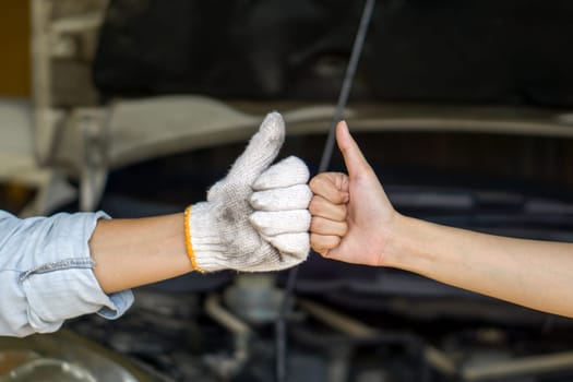 Close up two hands fist bump and thumb up showing success and good teamwork, stand in front of a car with an open hood.