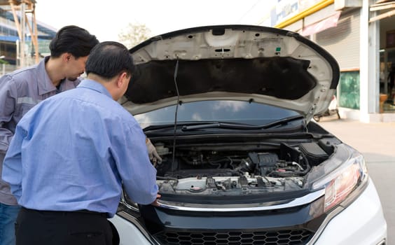 Two guys are standing by a car with the hood open, staring at the engine inside. Back view