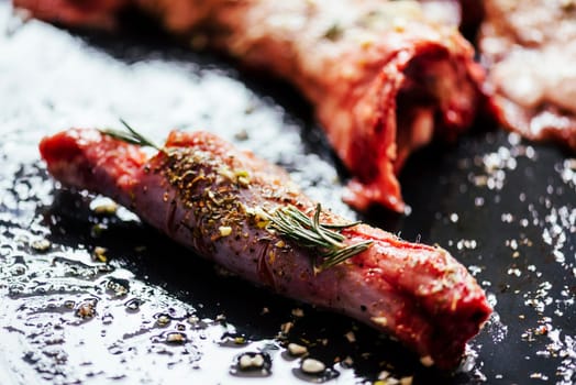 Lamb meat bbq preparation. Closeup of lamb chops with spices and rosemary on black rustic plate. Restaurant cuisine barbecue dish.