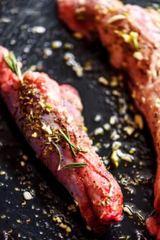 Lamb meat bbq preparation. Closeup of lamb chops with spices and rosemary on black rustic plate. Restaurant cuisine barbecue dish.