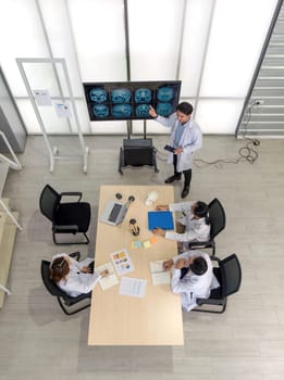 Group of doctor in white gown, discussing brain scans on large monitor in a meeting room. High angle view