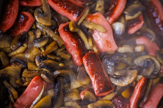 closeup view of roasting cut champignon mushrooms and sausages.