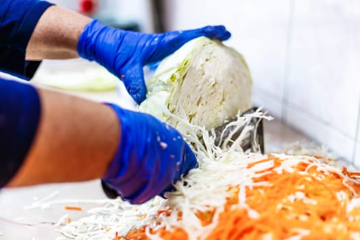 hands in blue gloves cutting cabbage with special double blade slit cabbage shredder knife during sauerkraut preparation