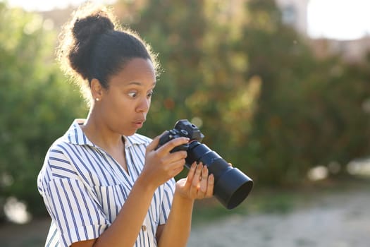 Surprised black photograper checking result on mirrorless camera in a park