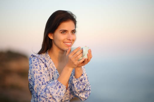 Happy woman contemplating views holding coffee mug at sunset on the beach