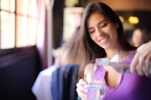 Happy woman filling a glass with water in a restaurant interior