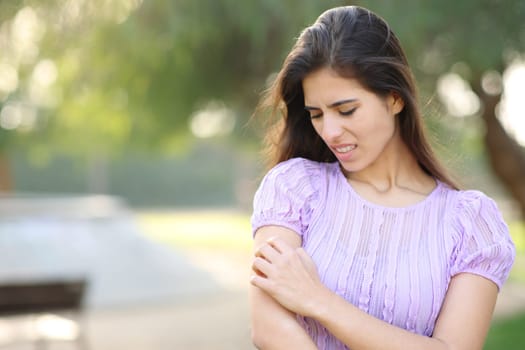 Woman scratching arm standing in a park in summer season
