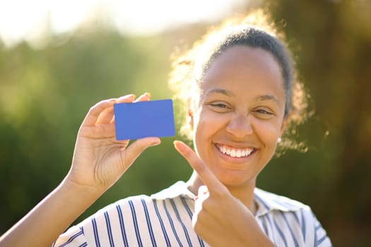 Front view portrait of a happy black buyer showing blank credit card in a park