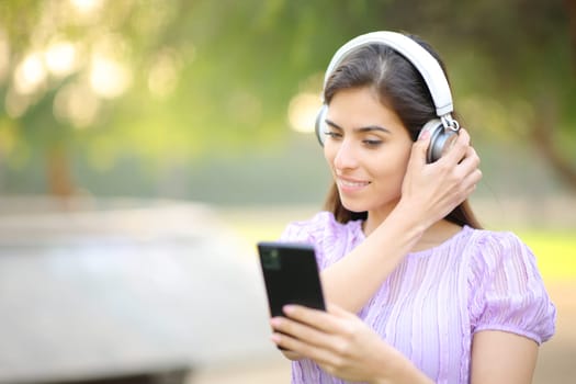 Woman putting headphone watching phone content in a park