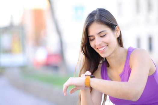 Happy woman using her smartwath sitting on a bench in the street