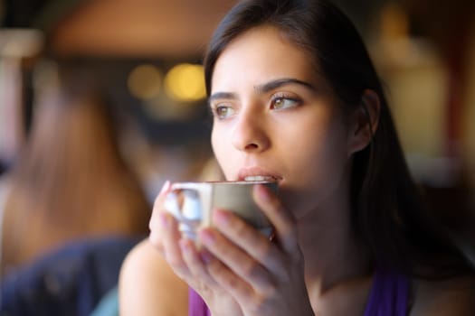 Pensive woman drinking coffee looking away in a restaurant