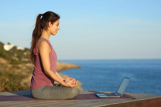 Yogi learning yoga watching video tutorial on laptop on the beach