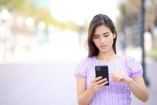 Front vire of a woman walking using cell phone in the street