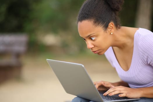 Shocked black woman checking laptop content sitting in a park