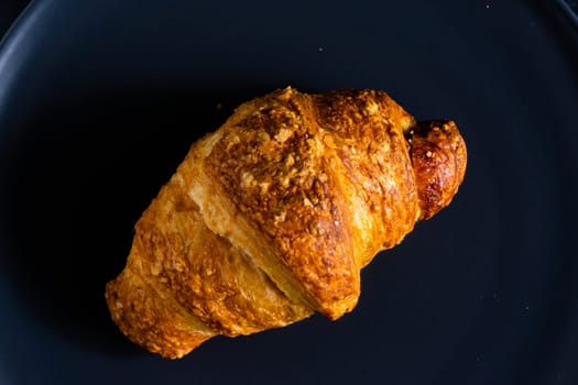 Freshly backed french croissant shiny in the rays of morning sun, dark background, kitchen