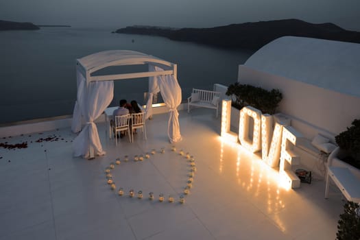 Imerovigli, Santorini, Greece - July 1, 2021: On a romantic evening, a couple admires the sunset in Santorini from the terrace