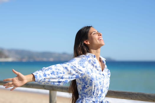 Happy woman outstretching arms celebrating a good day on the beach