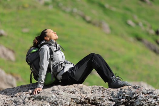 Hiker resting and relaxing with closed eyes sitting on a rock in the mountain