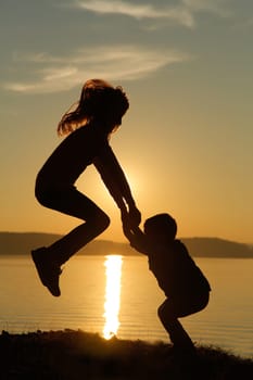 A charming silhouette of joyful children happily playing and splashing by the shimmering water at sunset